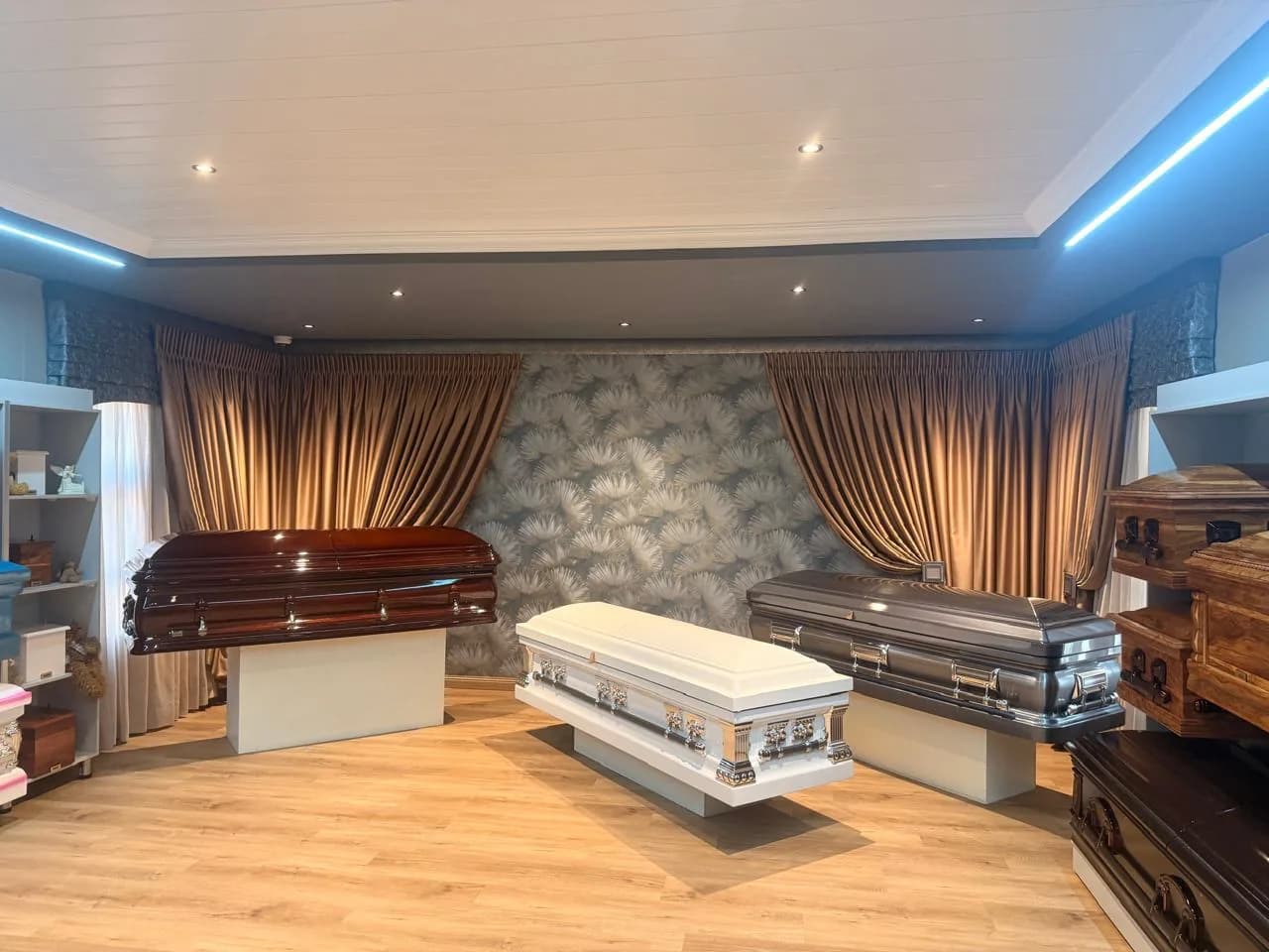 Funeral parlour display room with curtains, wallpaper, lighting and wall units