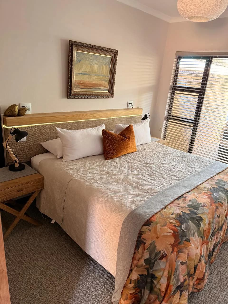 Bloemfontein bedroom with a timber and upholstered headboard, integrated LED lighting, slatted blinds and a floral bed runner