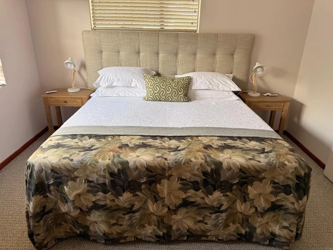 Bloemfontein bedroom with a wide upholstered headboard, timber bedside tables, reading lamps and a floral bed throw