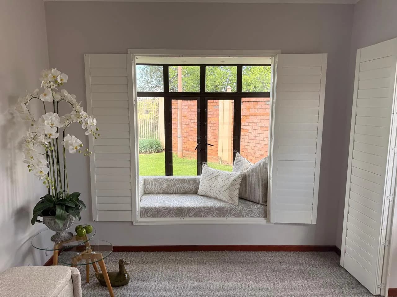 Bloemfontein window seat with shutters, neutral cushions, a glass side table and floral decor