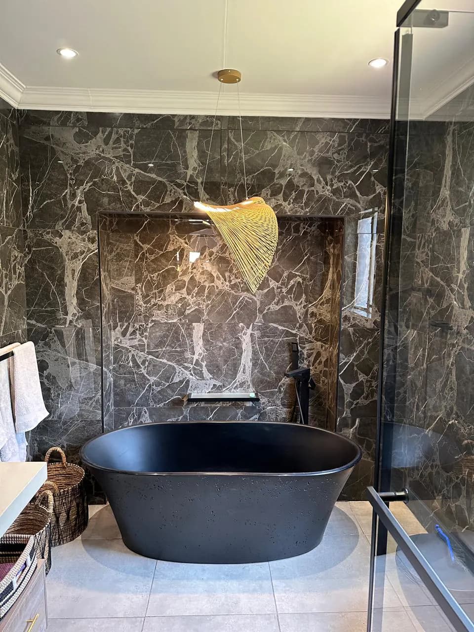 Bloemfontein residence bathroom with a black freestanding bath, dark stone-look wall finishes and sculptural pendant lighting