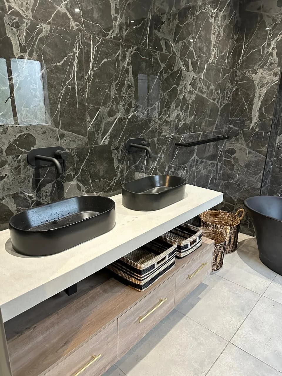 Bloemfontein bathroom with dark stone-look walls, twin black basins, a fitted vanity and woven baskets