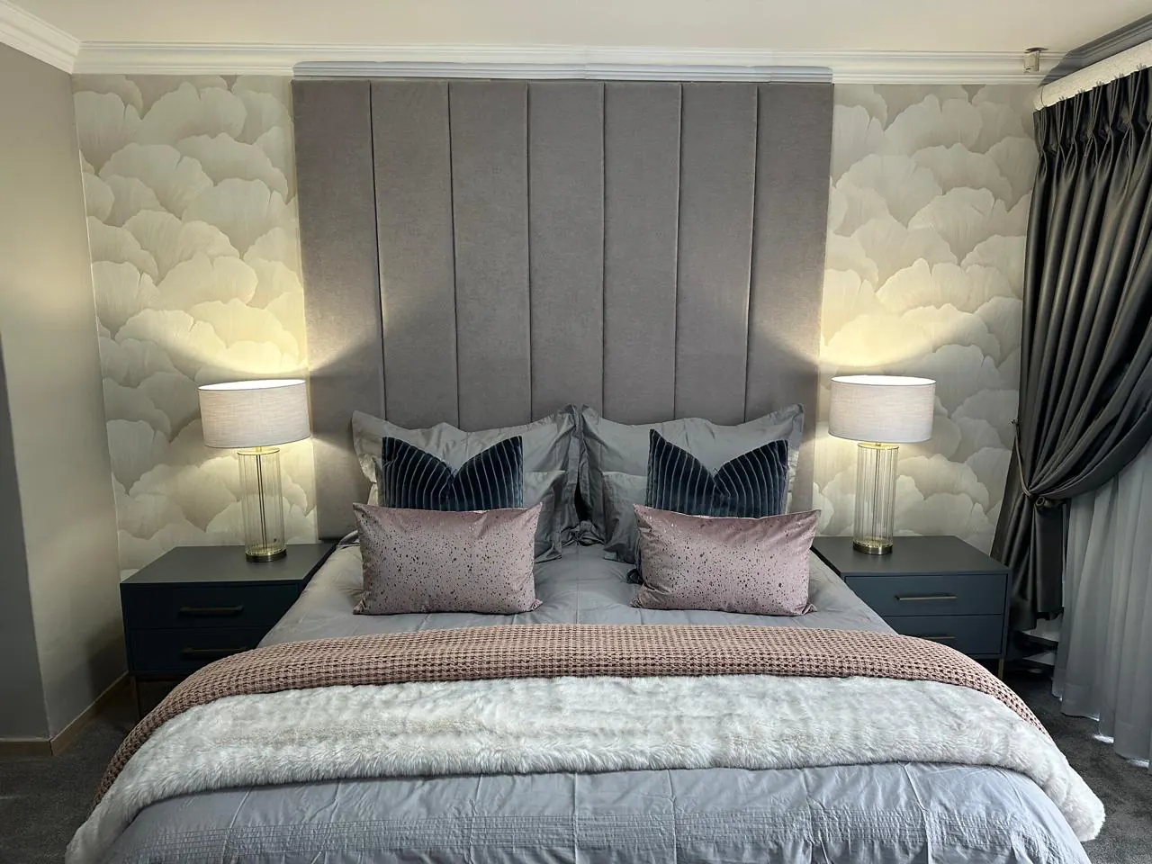Bloemfontein residence bedroom with a tall upholstered headboard, botanical wallpaper, layered bedding, bedside lamps and curtains