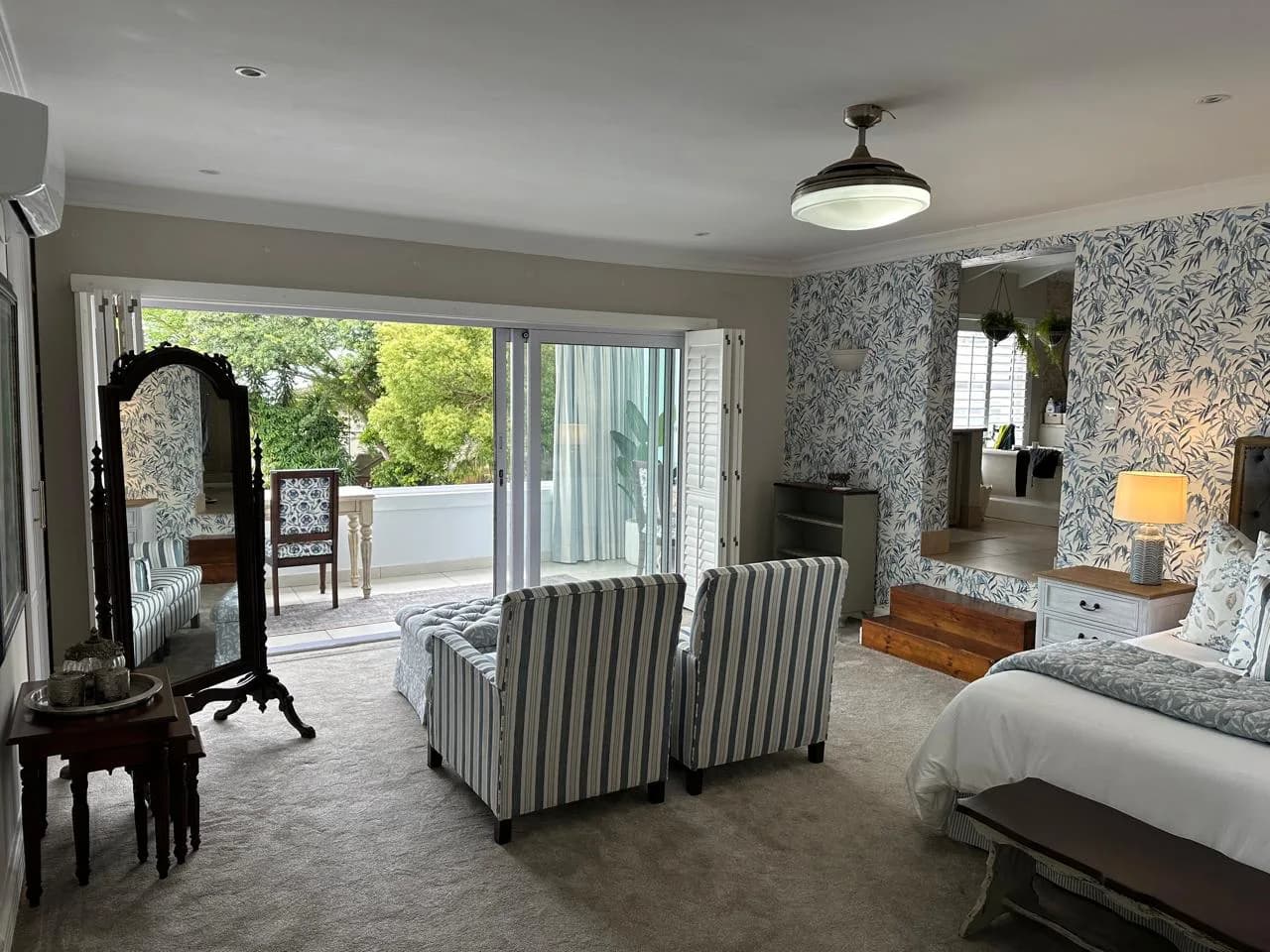 Wide view of the Durban bedroom with striped chairs, an ottoman, mirrors and wallpaper