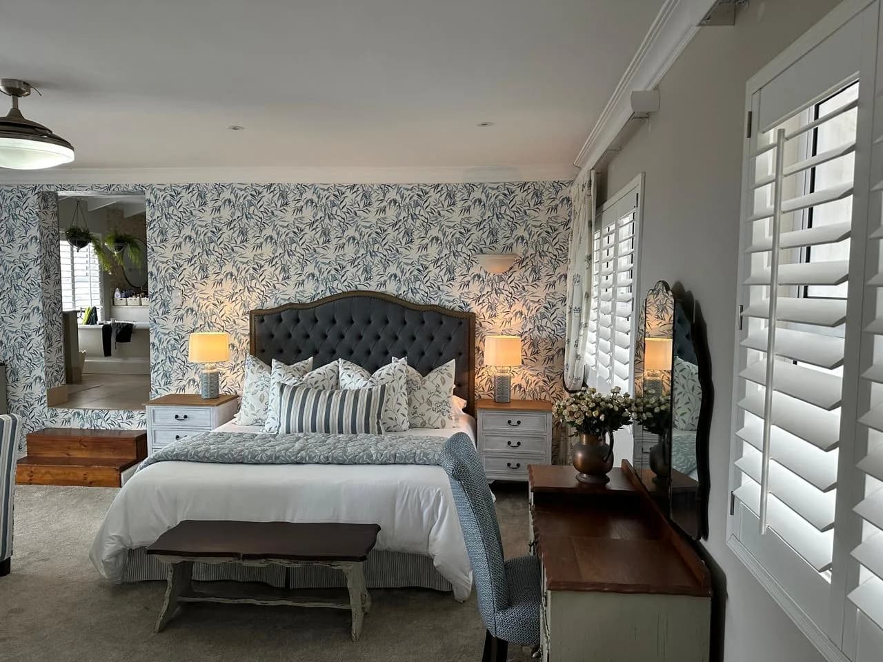Durban bedroom with botanical wallpaper, plantation shutters, a curved upholstered headboard, mirrors and bedside lamps