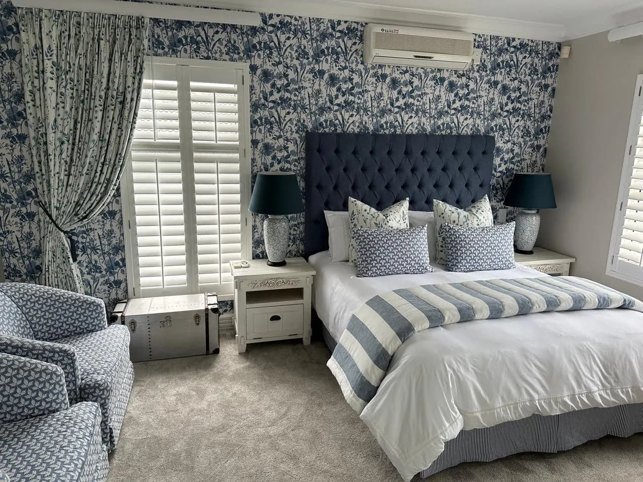Durban bedroom with blue botanical wallpaper, matching curtains, plantation shutters, a buttoned headboard and layered bedding