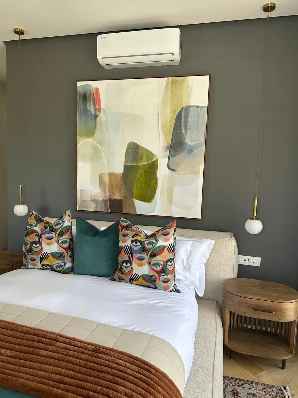 Paarl bedroom with abstract artwork, colourful cushions, an upholstered bed, timber side tables and suspended pendant lights