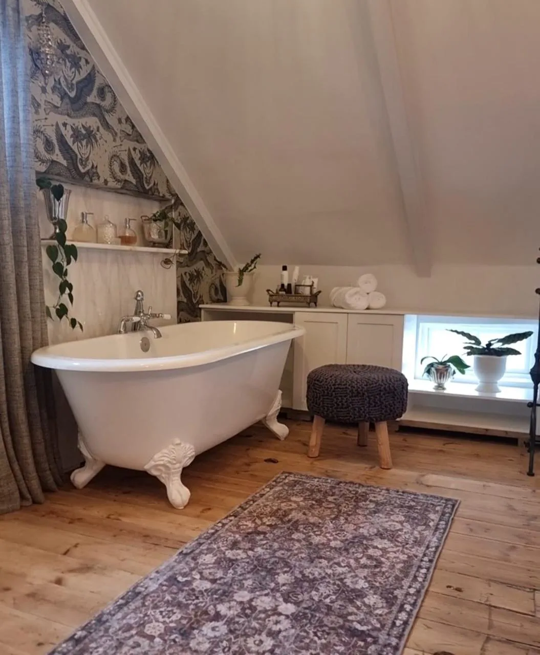 Riebeeck Kasteel bathroom with a freestanding bath, wallpaper, curtains, ottoman and patterned rug