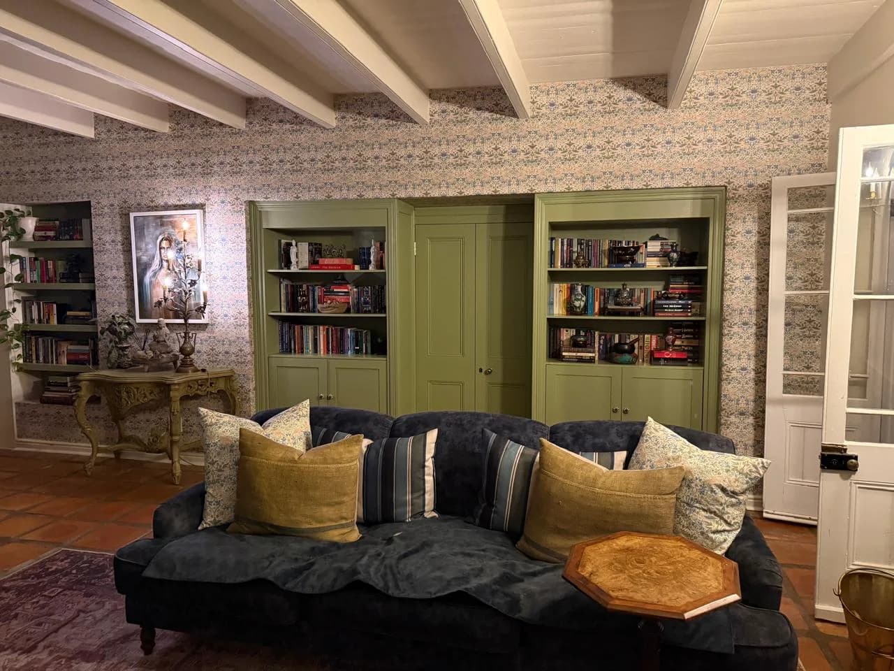 Riebeeck Kasteel living room with olive painted bookcases, patterned wallpaper, a dark upholstered sofa and layered cushions
