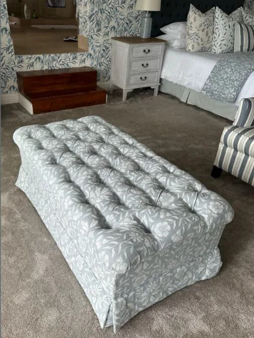 Leaf-patterned, button-tufted upholstered ottoman in a coordinated bedroom interior.