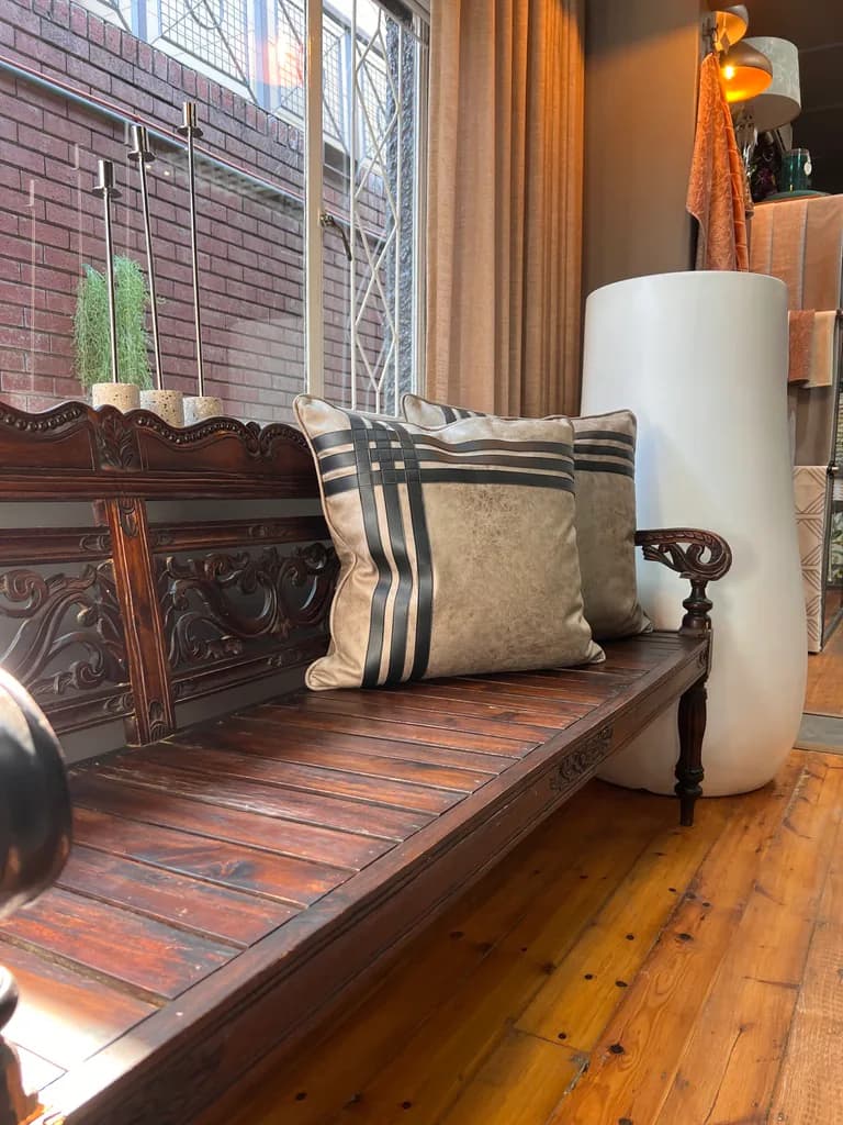 Carved wooden bench with cushions, curtains and showroom decor.