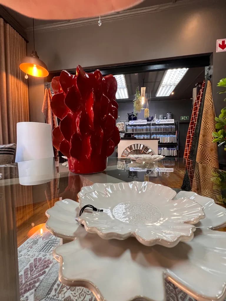 Decorative bowl and red vase displayed on a glass showroom table.