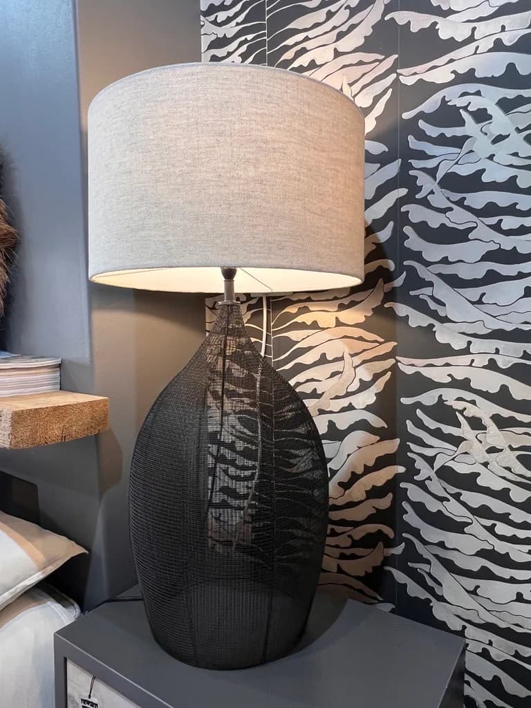 Black table lamp displayed against patterned wallpaper in the showroom.