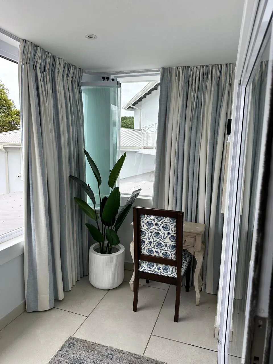 Finished curtains installed around a bright patio room with a chair and plant.