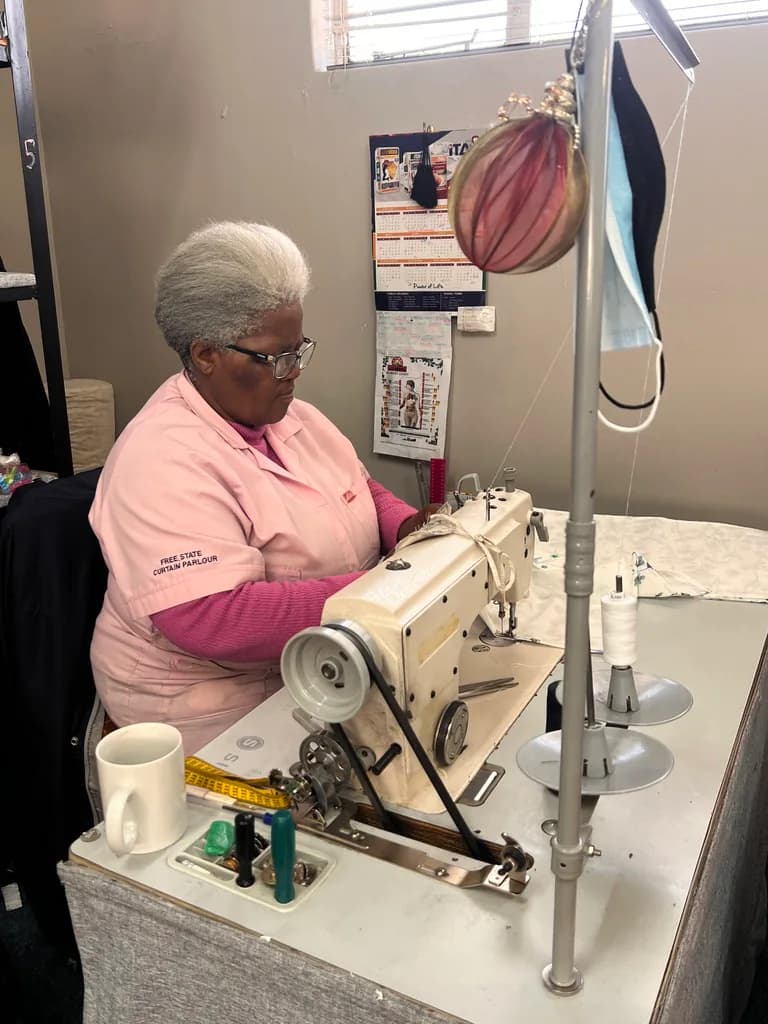 A seamstress sewing fabric at a workshop sewing machine.